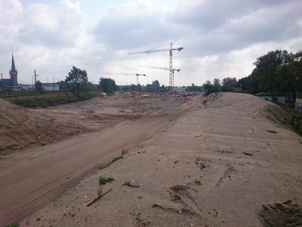 Blick vom Bereich der Teilfläche 05 – Naturnaher Bereich in Richtung Teilfläche 04 – Spielband. Im Hintergrund ist der Schulneubau zu sehen. Im Vordergrund befinden sich z. Zt. noch Erdmieten des Schulbaus.
